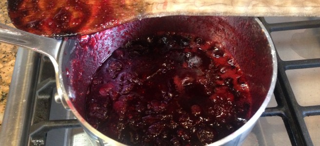 pot with cranberry sauce bubbling on stove with wooden spoon on top