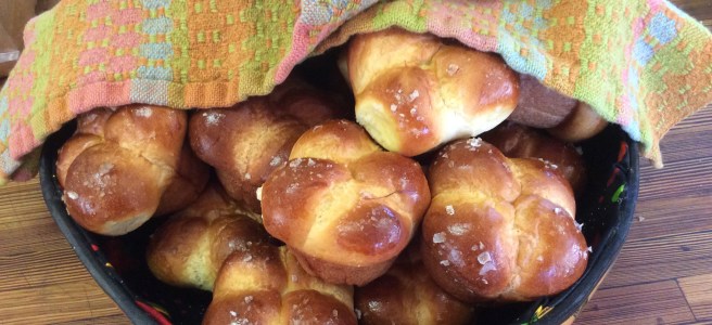 a bowl of rolls with course salt on top covered with a colorful towel