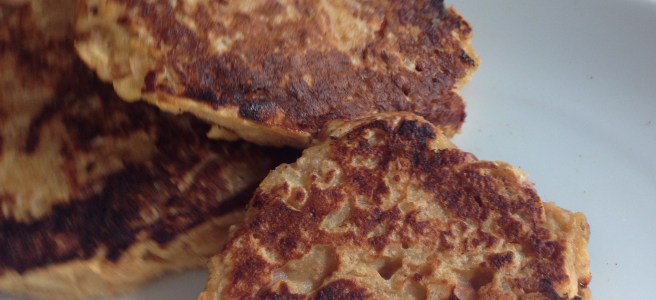 three browned pancakes on a plate with fingers taking the one top left